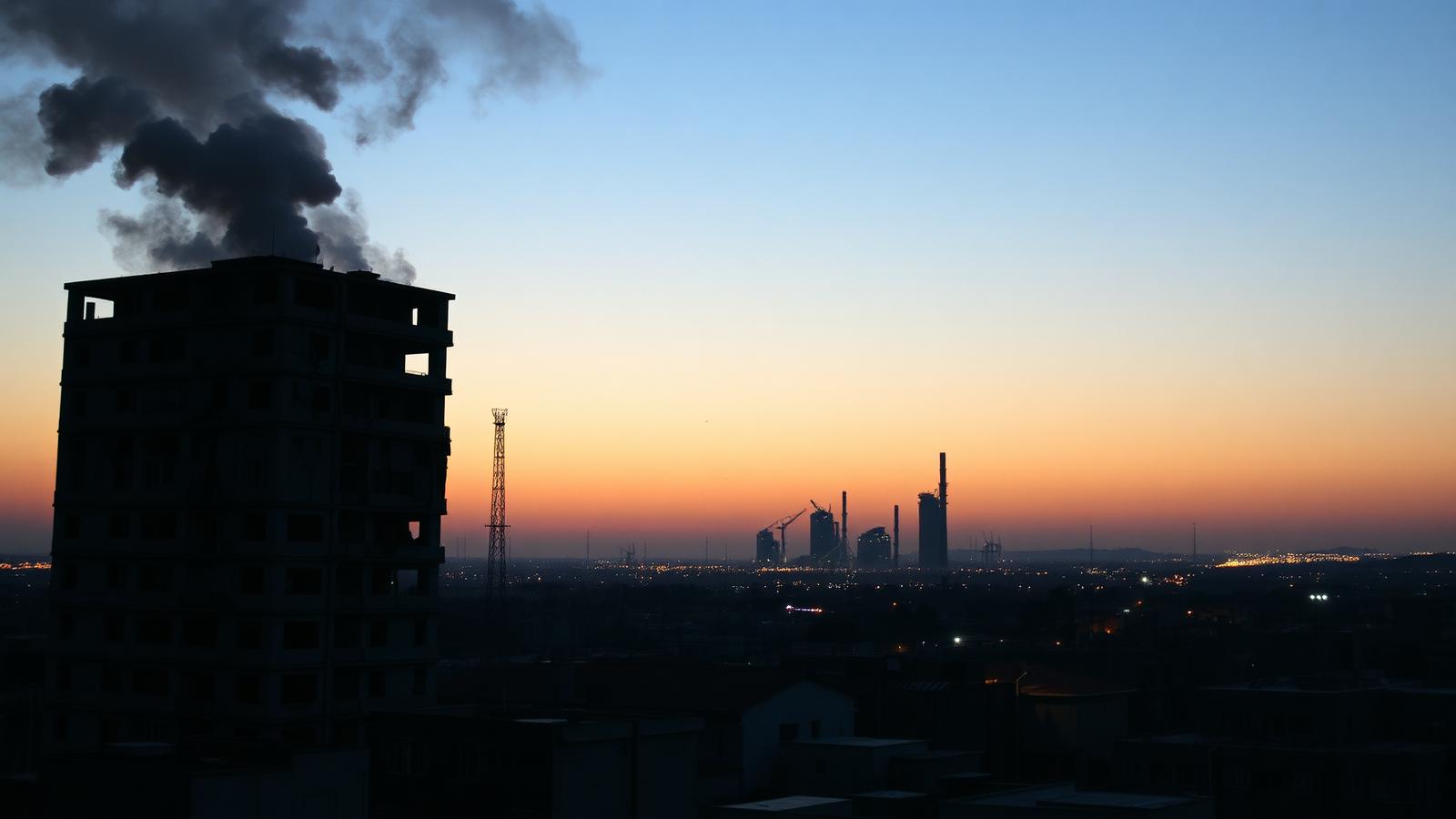 Smoke rises over a city skyline at dusk.